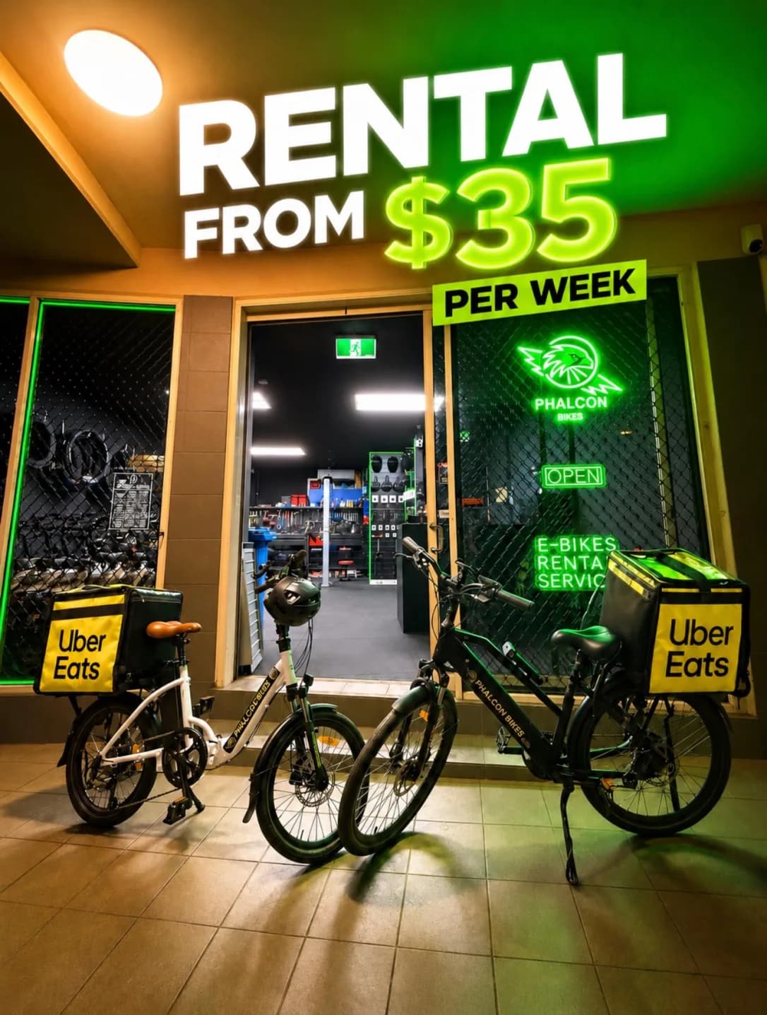 Two Phalcon rental e-bikes with delivery bags outside the lit Chippendale shopfront at night